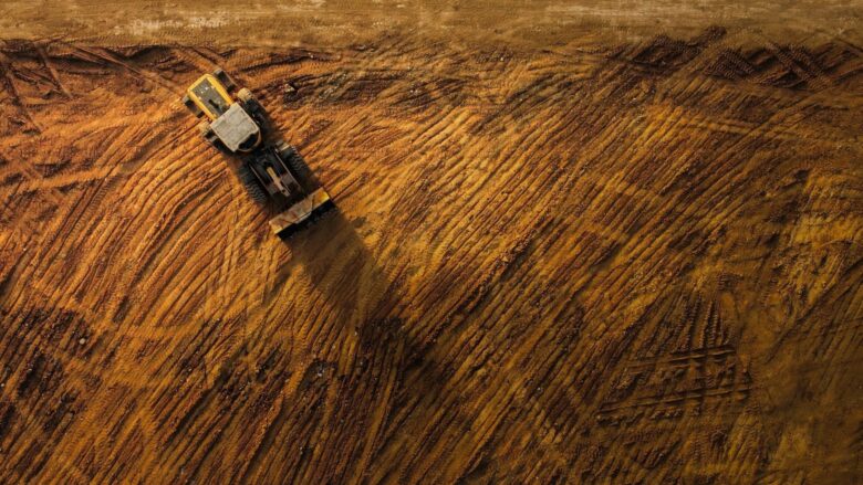 Top-down view of a track-packing machine crossing a muddy dirt surface