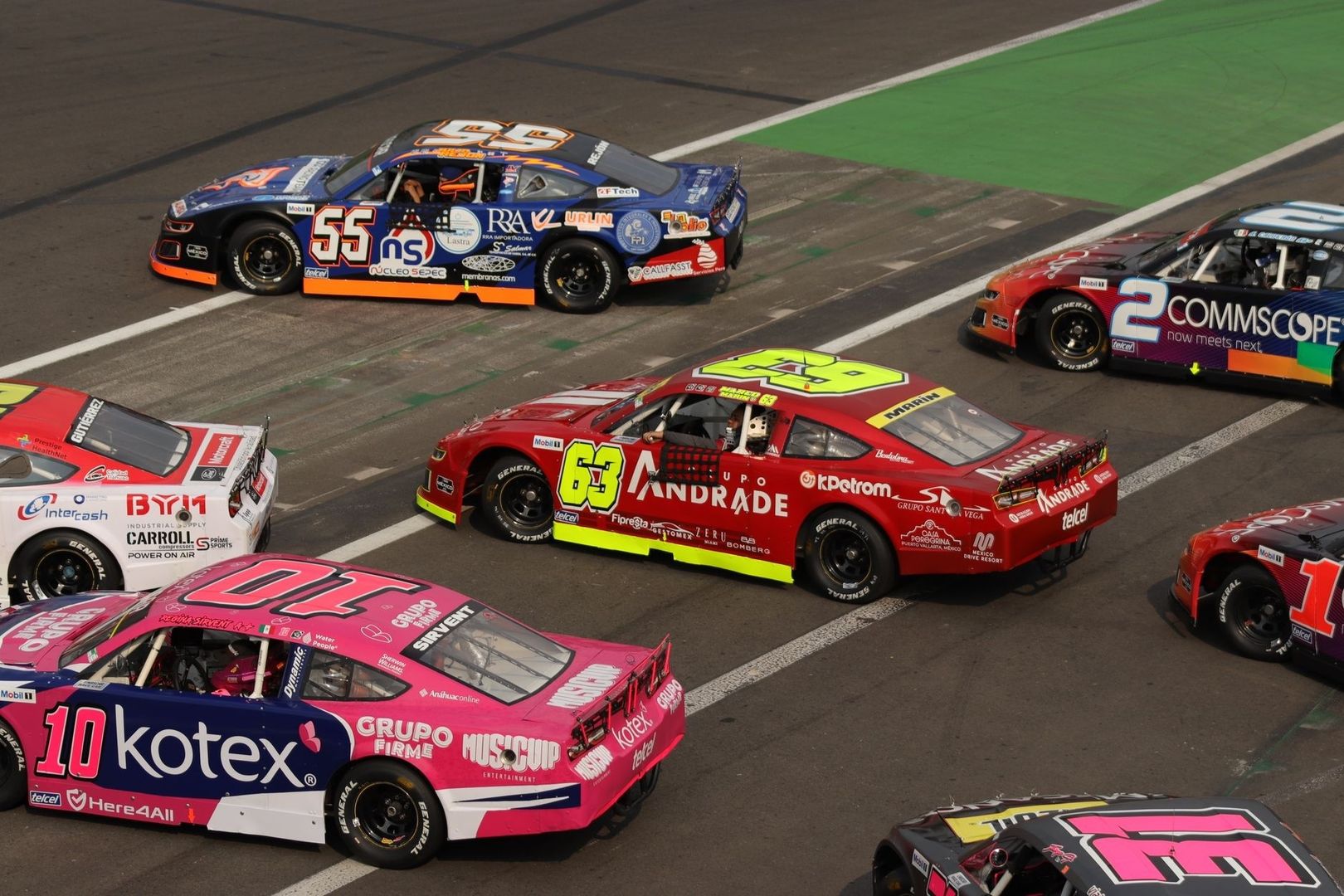 Stock cars line up on a paved racing grid before a start